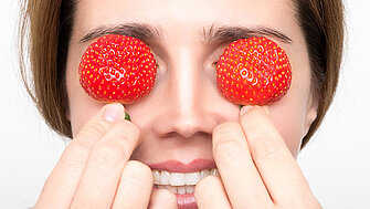 Ein Frau hält sich zwei Erdbeeren vor die Augen.